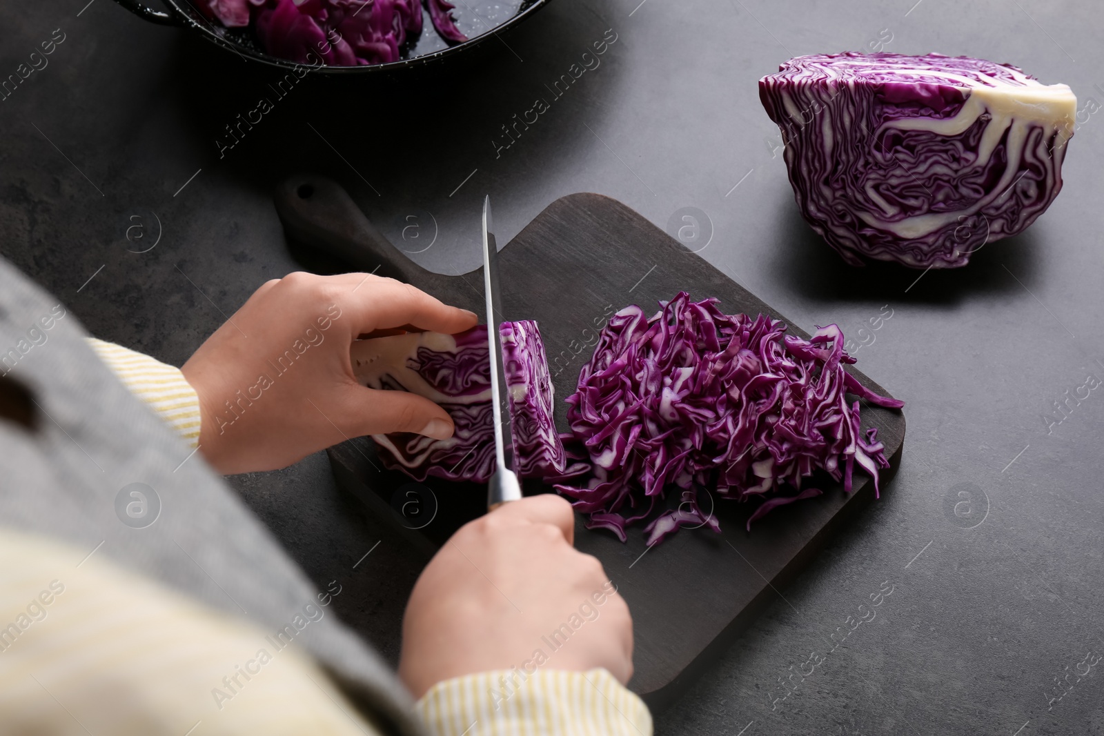 Photo of Woman cutting fresh red cabbage at black table, closeup