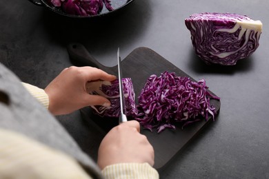 Photo of Woman cutting fresh red cabbage at black table, closeup