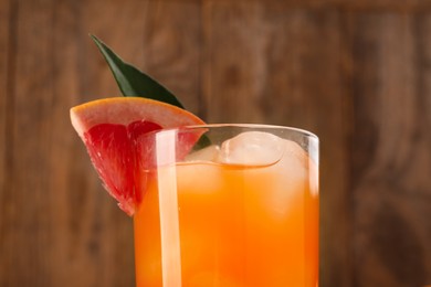 Photo of Tasty grapefruit drink with ice, slice of fruit and leaf in glass on blurred background, closeup