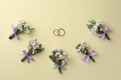 Small stylish boutonnieres and rings on beige background, flat lay