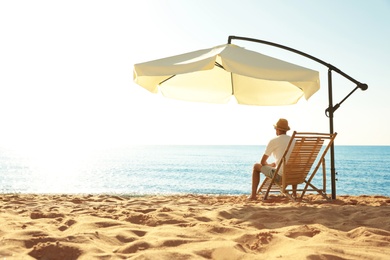 Photo of Man relaxing on deck chair at sandy beach. Summer vacation