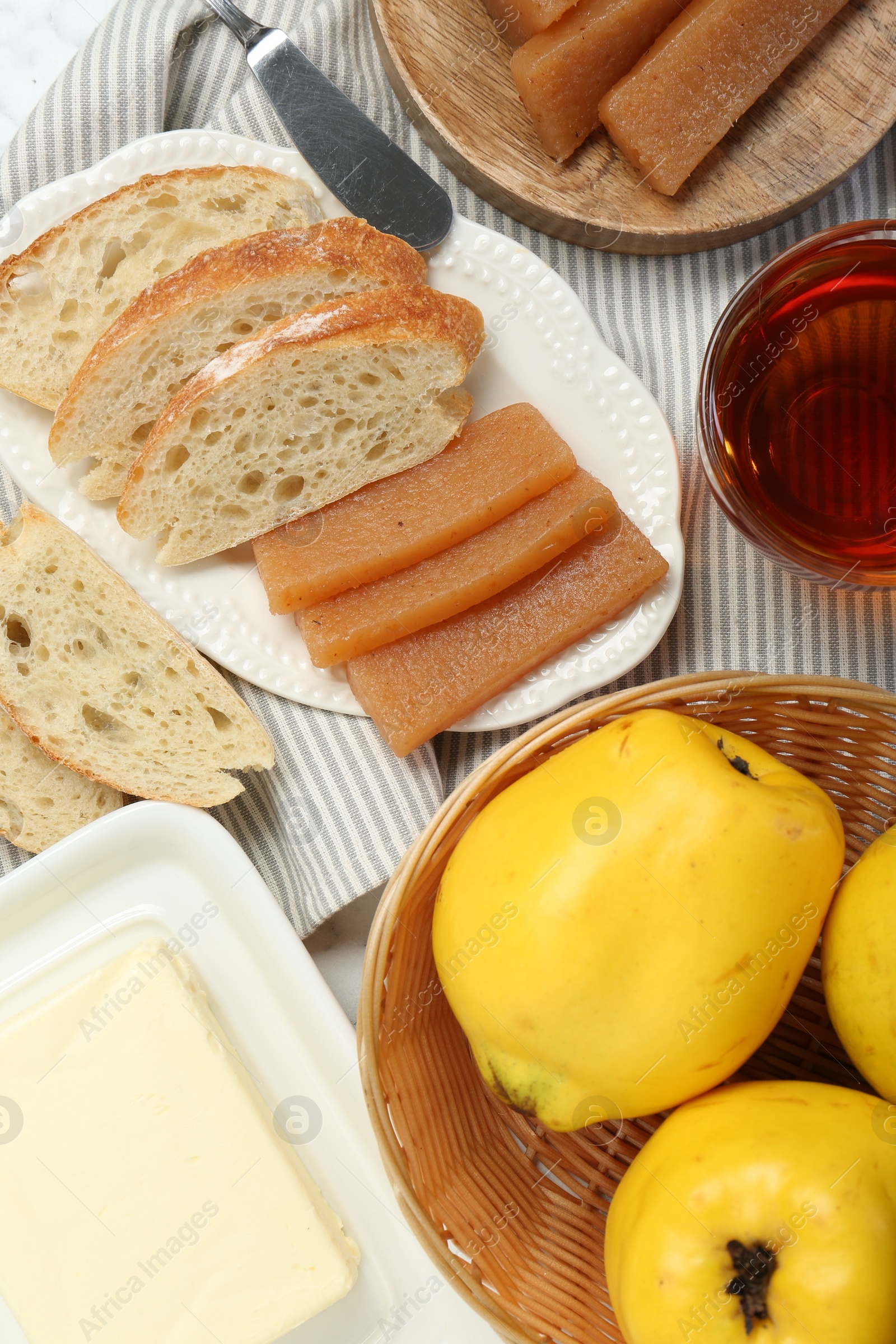 Photo of Delicious quince paste, bread, butter, cup of tea and fresh fruits on table, flat lay