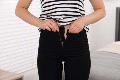 Photo of Woman trying to fit into her black jeans at home, closeup