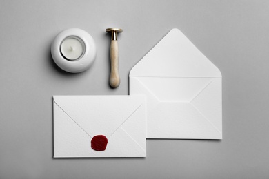 Photo of Envelopes with wax seal, candle and stamp on grey background, flat lay