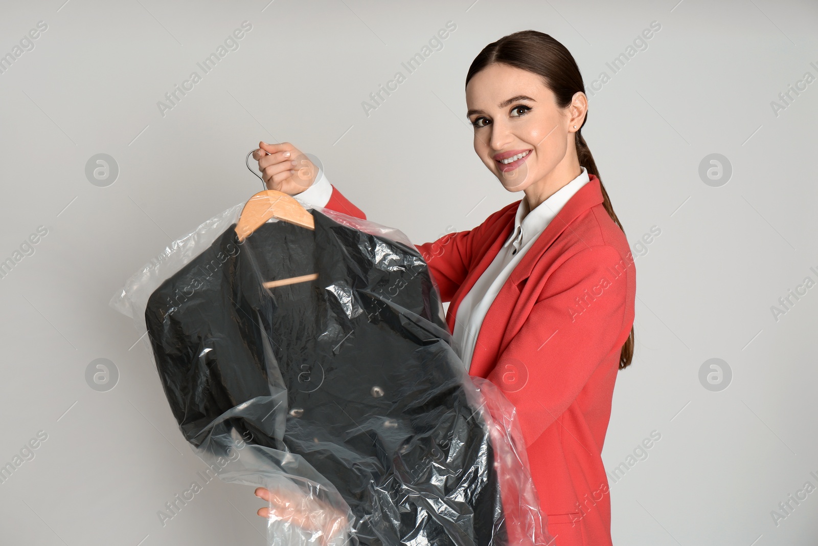 Photo of Young woman holding hanger with dress on light grey background. Dry-cleaning service