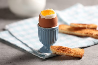Photo of Tasty boiled chicken egg with toasted bread on grey table, closeup