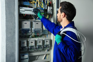 Photo of Electrician with wires switching off circuit breakers in fuse box indoors