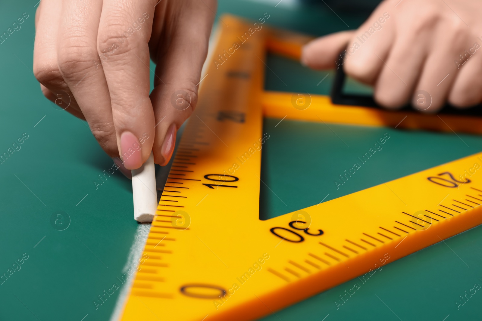 Photo of Woman drawing with chalk and triangle ruler on green board, closeup