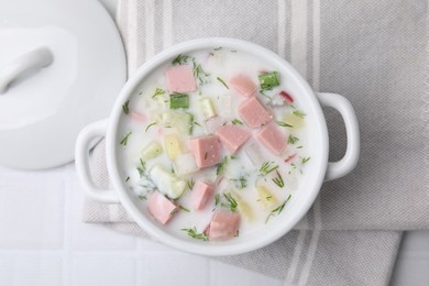 Delicious cold summer soup (okroshka) with boiled sausage in pot on white tiled table, top view