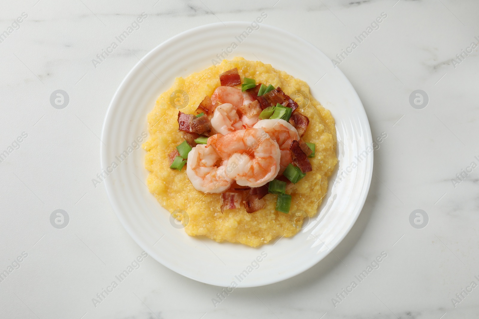 Photo of Plate with fresh tasty shrimps, bacon, grits and green onion on white marble table, top view