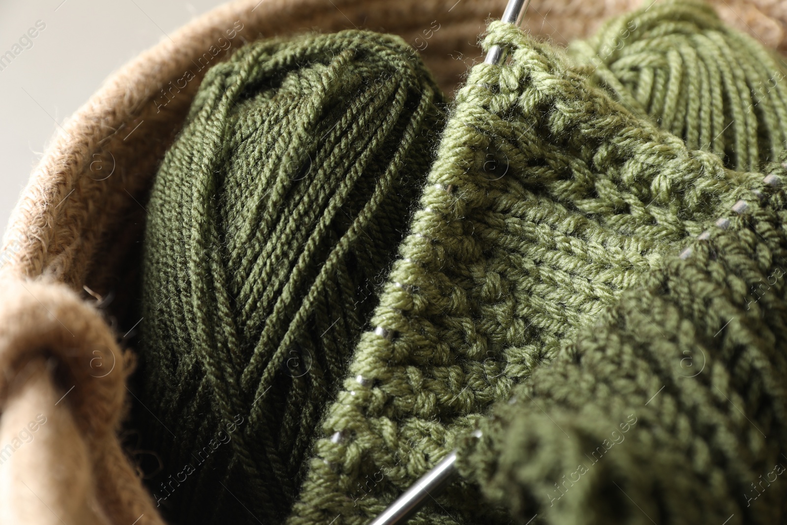 Photo of Green knitting, needles and soft yarns on light background, closeup