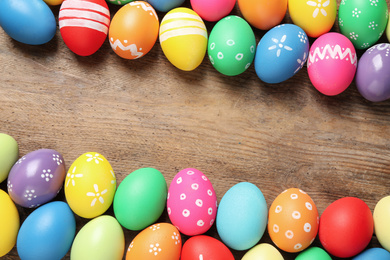 Photo of Frame made with colorful Easter eggs on wooden background. Space for text