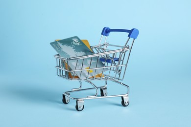 Photo of Small metal shopping cart with credit cards on light blue background