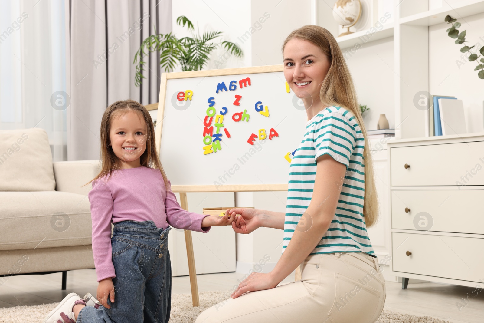 Photo of Mom teaching her daughter alphabet with magnetic letters at home