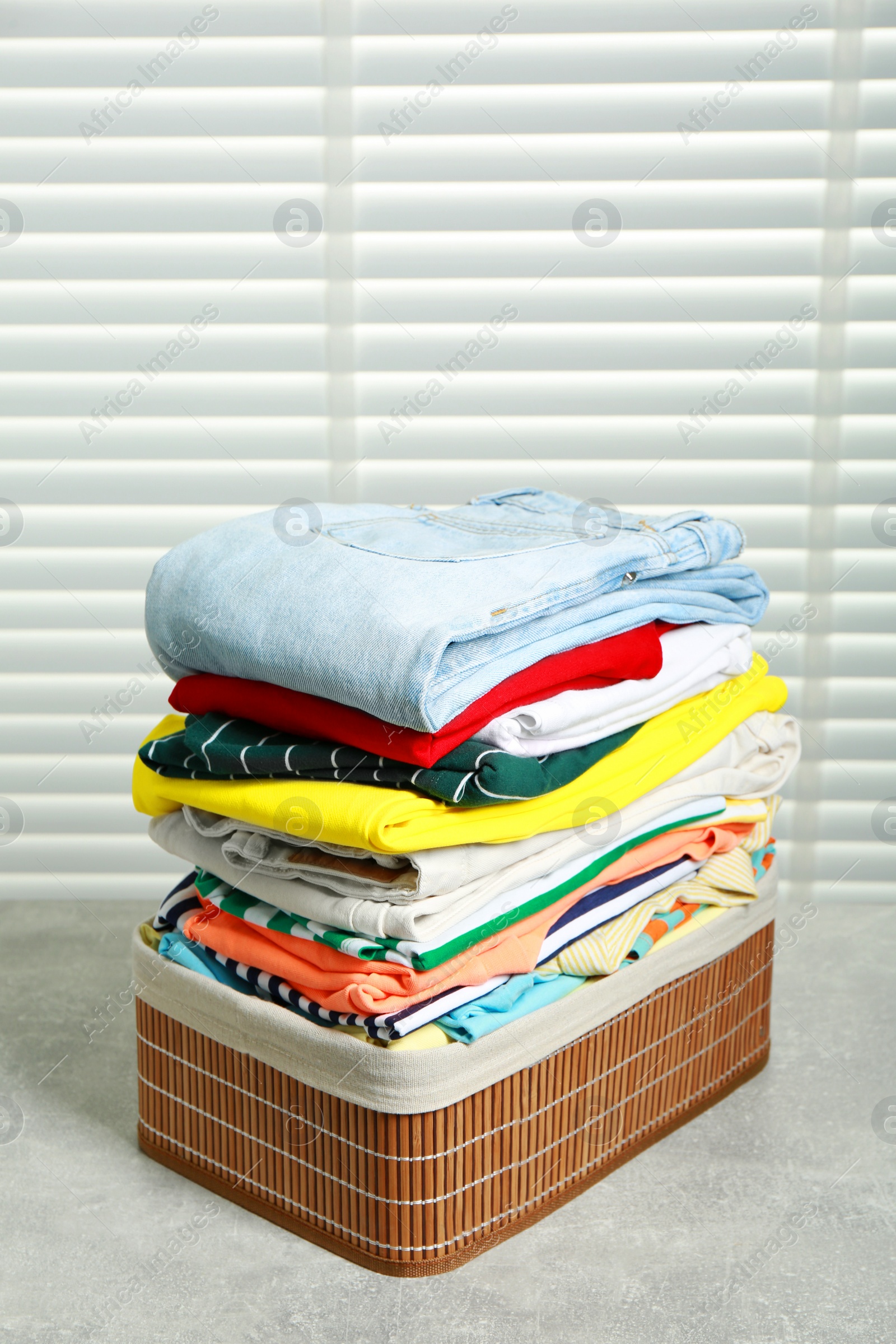 Photo of Laundry basket with clean clothes on light grey table indoors