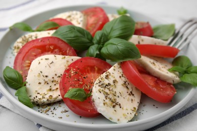 Photo of Caprese salad with tomatoes, mozzarella, basil and spices on table, closeup