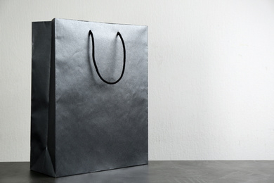 Photo of Black shopping paper bag on table against light background. Space for text