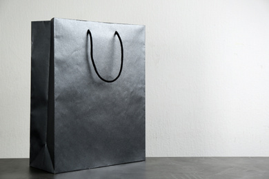 Black shopping paper bag on table against light background. Space for text