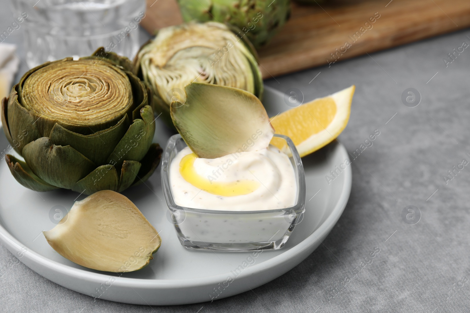 Photo of Delicious cooked artichokes with tasty sauce served on grey table, closeup