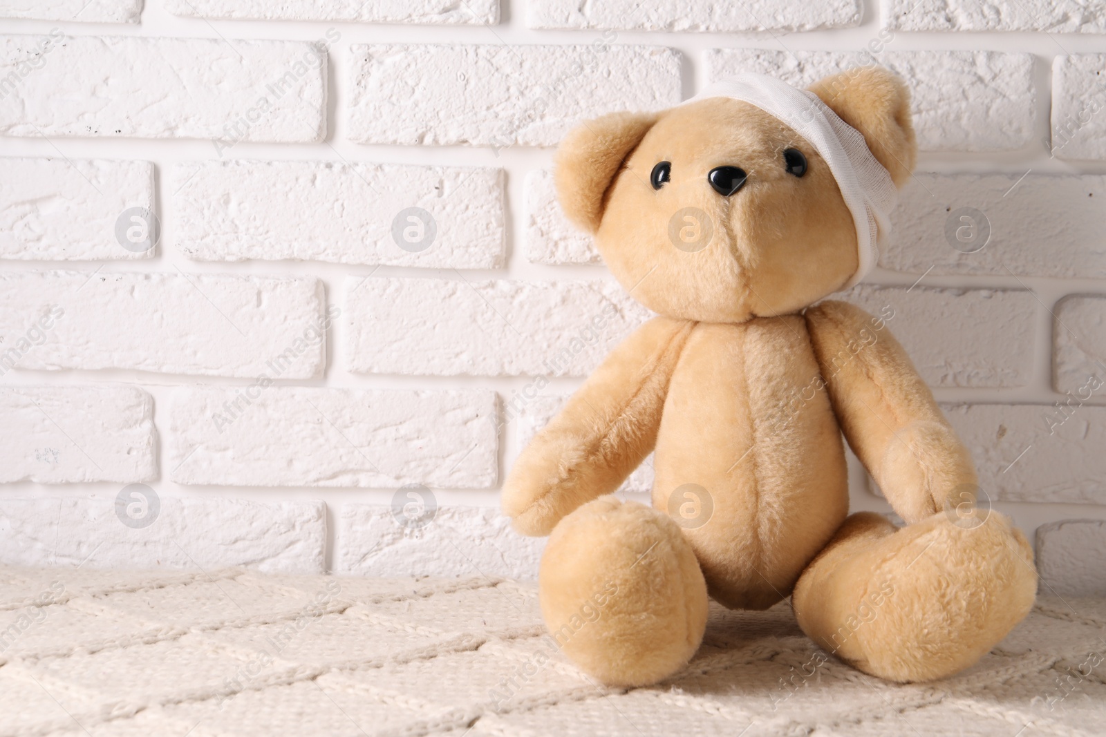 Photo of Toy bear with bandage on soft surface near white brick wall, space for text