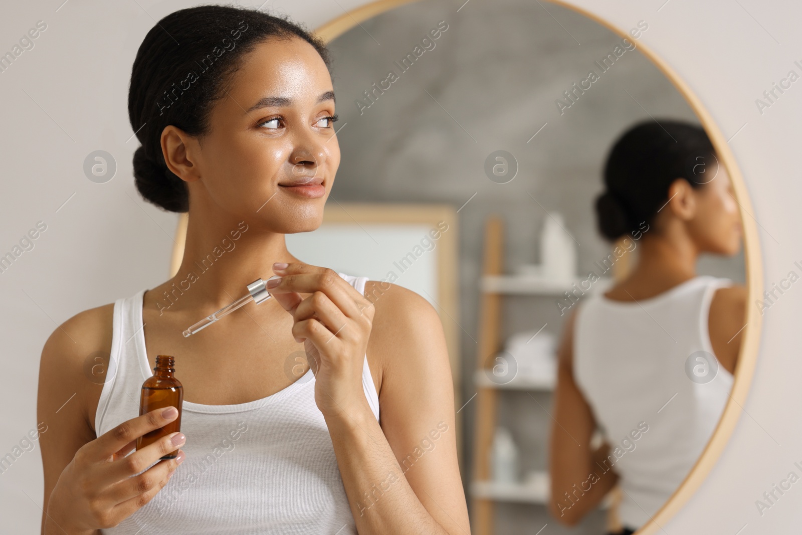 Photo of Beautiful woman with bottle of serum and dropper in bathroom. Space for text