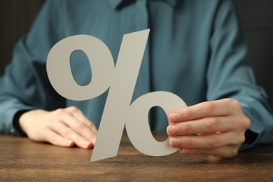 Photo of Woman holding percent sign at wooden table, closeup