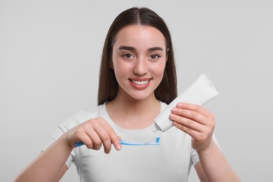 Photo of Happy young woman squeezing toothpaste from tube onto plastic toothbrush on white background