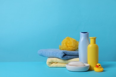 Photo of Baby cosmetic products, bath duck, sponge and towels on light blue background. Space for text