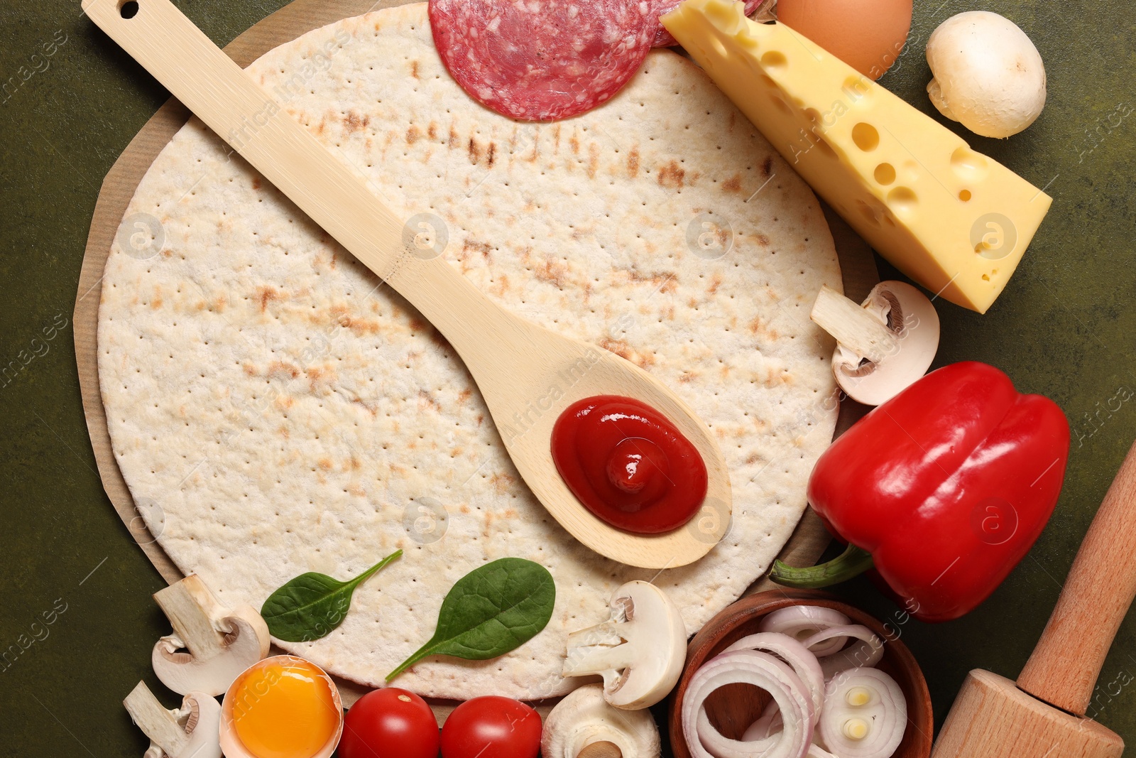 Photo of Pizza base, spoon with tomato sauce and products on green textured table, flat lay