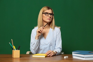 Portrait of beautiful teacher sitting at table near chalkboard