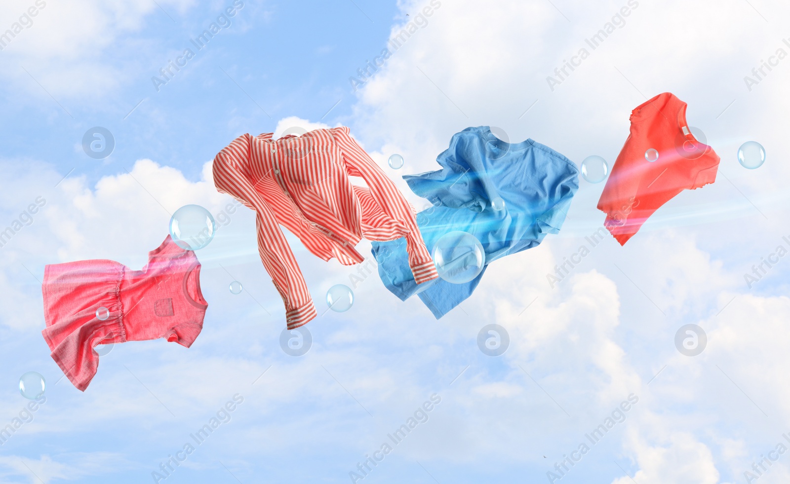 Image of Washing powder bubbles and clothes flying in blue cloudy sky