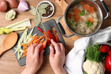 Photo of Woman cutting vegetables for bouillon at wooden table, top view