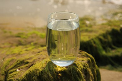 Photo of Glass of fresh water on stone with seaweed near sea
