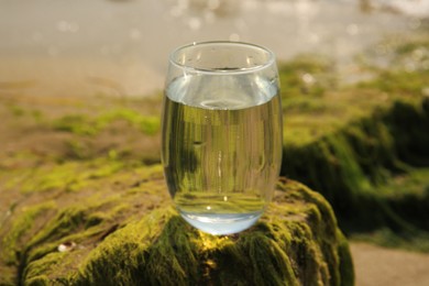 Glass of fresh water on stone with seaweed near sea