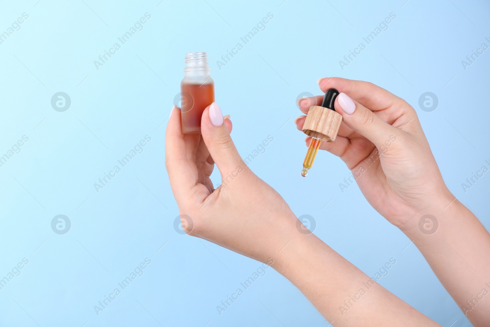 Photo of Woman applying essential oil onto wrist against light blue background, closeup