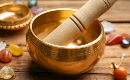 Photo of Golden singing bowl with mallet on wooden table, closeup. Sound healing