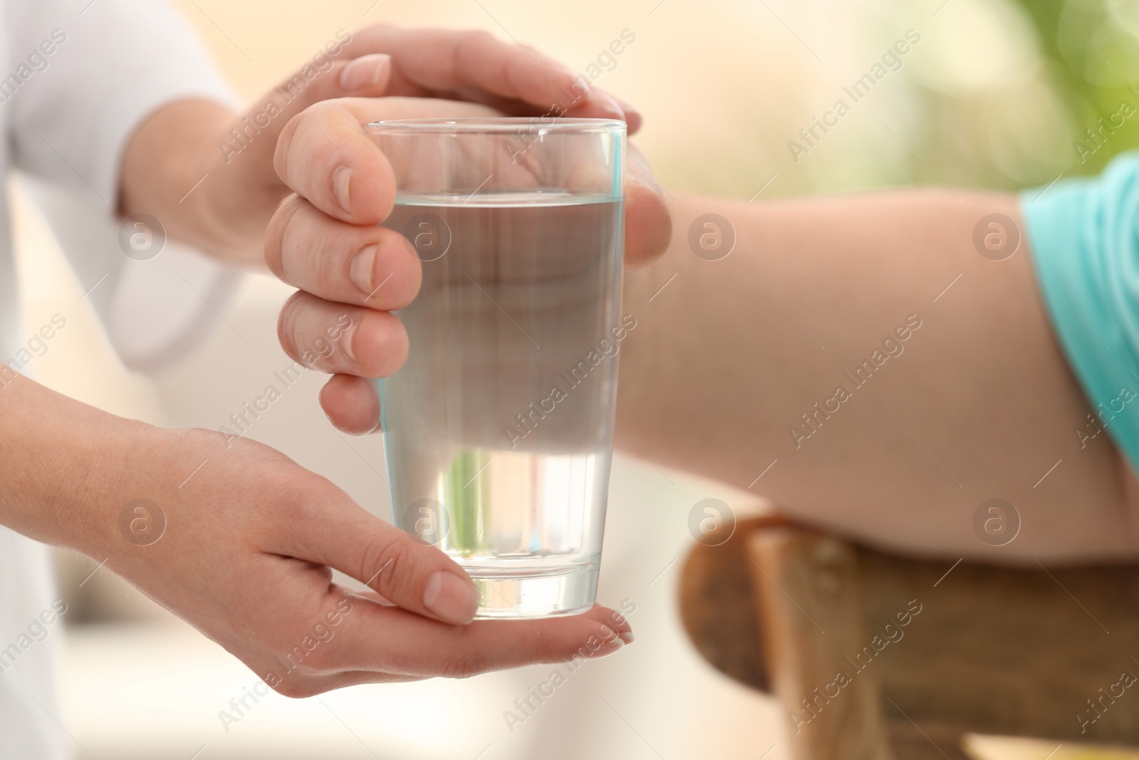 Photo of Nurse giving glass of water to elderly man indoors, closeup. Assisting senior generation