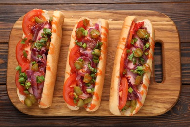 Tasty hot dogs with green onion, tomato, pickles and sauce on wooden table, top view