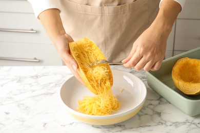 Photo of Woman scraping flesh of cooked spaghetti squash with fork in kitchen