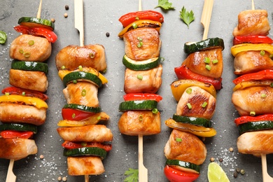 Photo of Delicious chicken shish kebabs with vegetables and herbs on grey table, flat lay