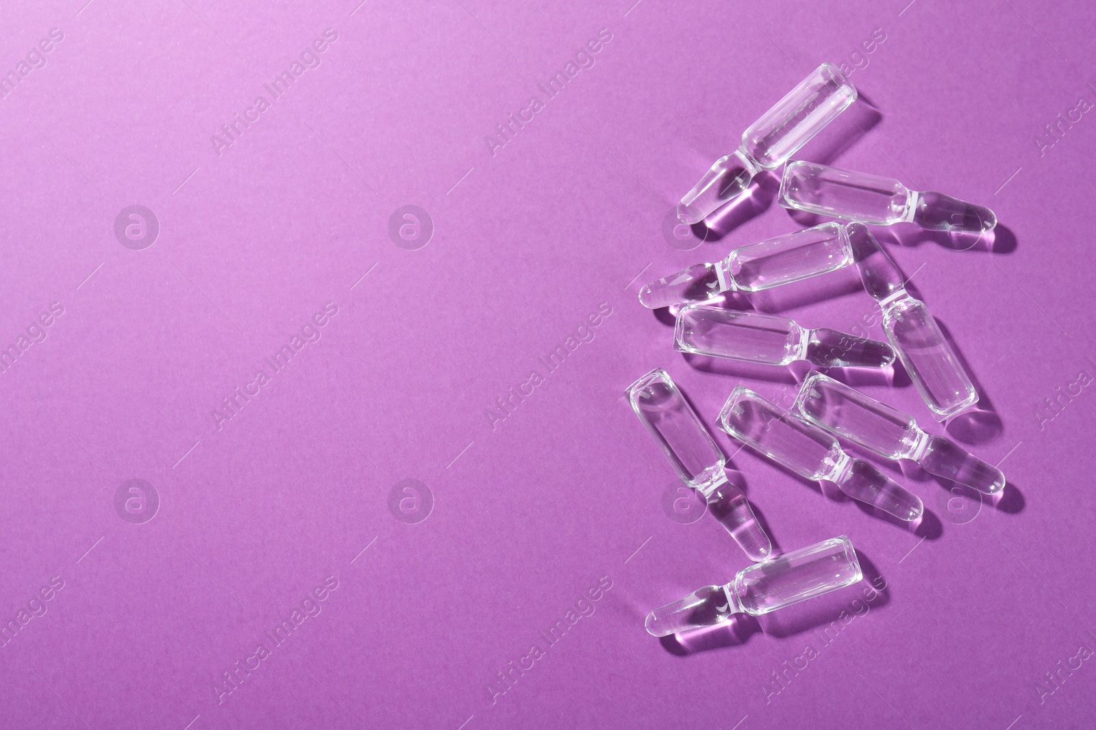 Photo of Glass ampoules with liquid on purple background, top view. Space for text