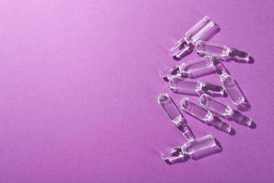 Photo of Glass ampoules with liquid on purple background, top view. Space for text