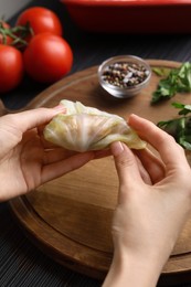 Woman preparing stuffed cabbage roll at table, closeup