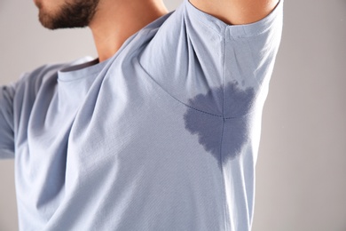 Photo of Sweaty man with stain on t-shirt against gray background, closeup. Using deodorant