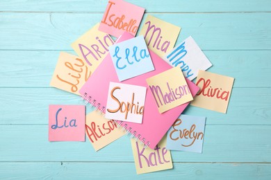 Photo of Paper notes with different baby names and notebook on light blue wooden table, flat lay
