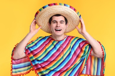 Young man in Mexican sombrero hat and poncho on yellow background