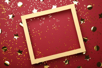 Photo of Wooden frame and confetti on red background, flat lay. Space for text