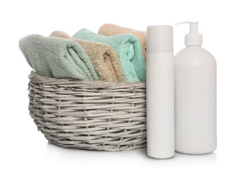 Photo of Soft towels in wicker basket and bottles of cosmetic products on white background