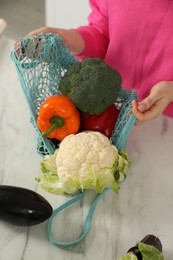 Woman with string bag of fresh vegetables at light marble table, above view