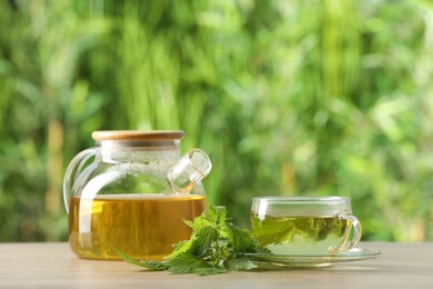 Photo of Aromatic nettle tea and green leaves on table outdoors